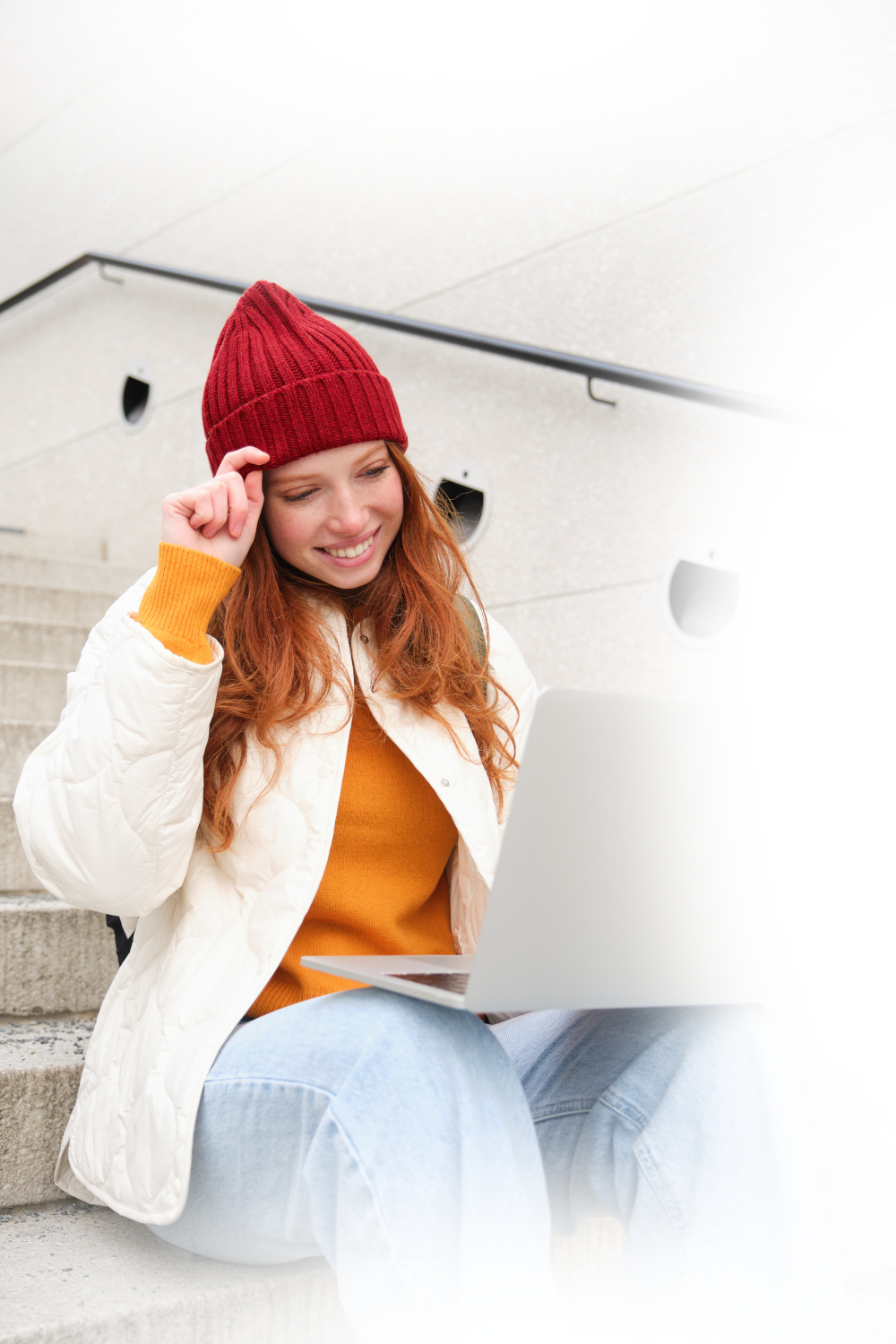 una-estudiante-pelirroja-sonriente-se-sienta-en-las-escaleras-al-aire-libre-y-usa-una-computadora-portatil-que-se-conecta-wifi-publico-en-la-ciudad-fundido1